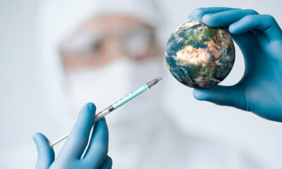 A person wearing personal protective equipment mimics injecting a vaccine into a module of earth.