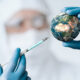 A person wearing personal protective equipment mimics injecting a vaccine into a module of earth.