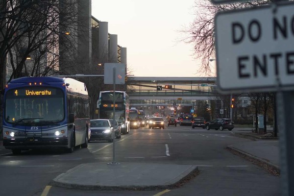 A view down a street. Several buses and cares are driving towards camera and less are driving away.