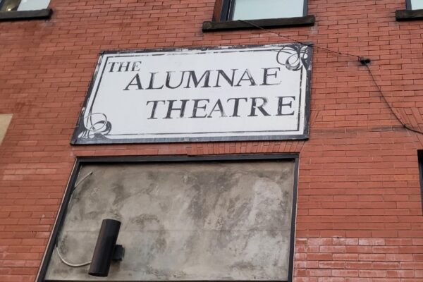 A sign saying "THE ALUMNAE THEATRE" on a brick wall