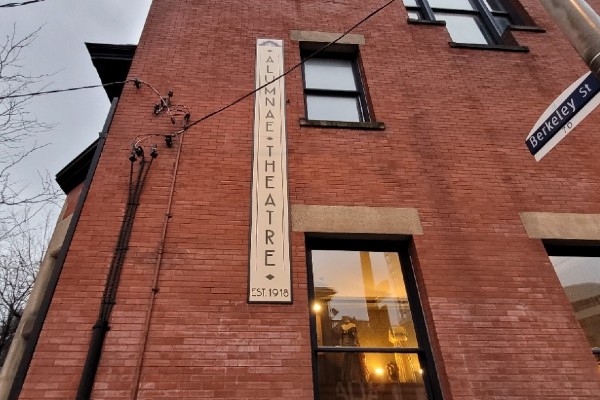 The side of a brick building with a vertical sign saying "ALUMNAE THEATRE - EST 1918"